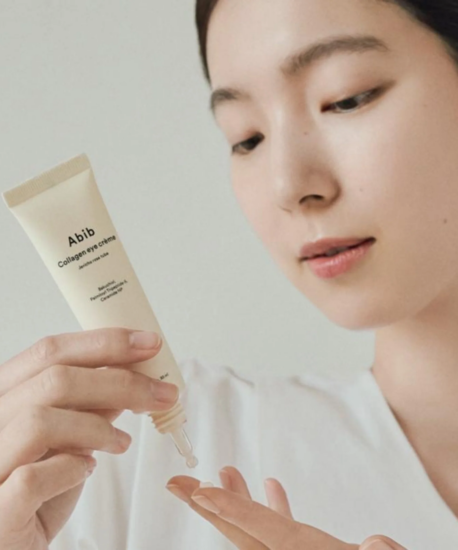 Décris l'image en français : ABIB Collagen Eye Cream Jericho Rose Tube 30ml d’Abib, main applique crème sur le visage, rose.