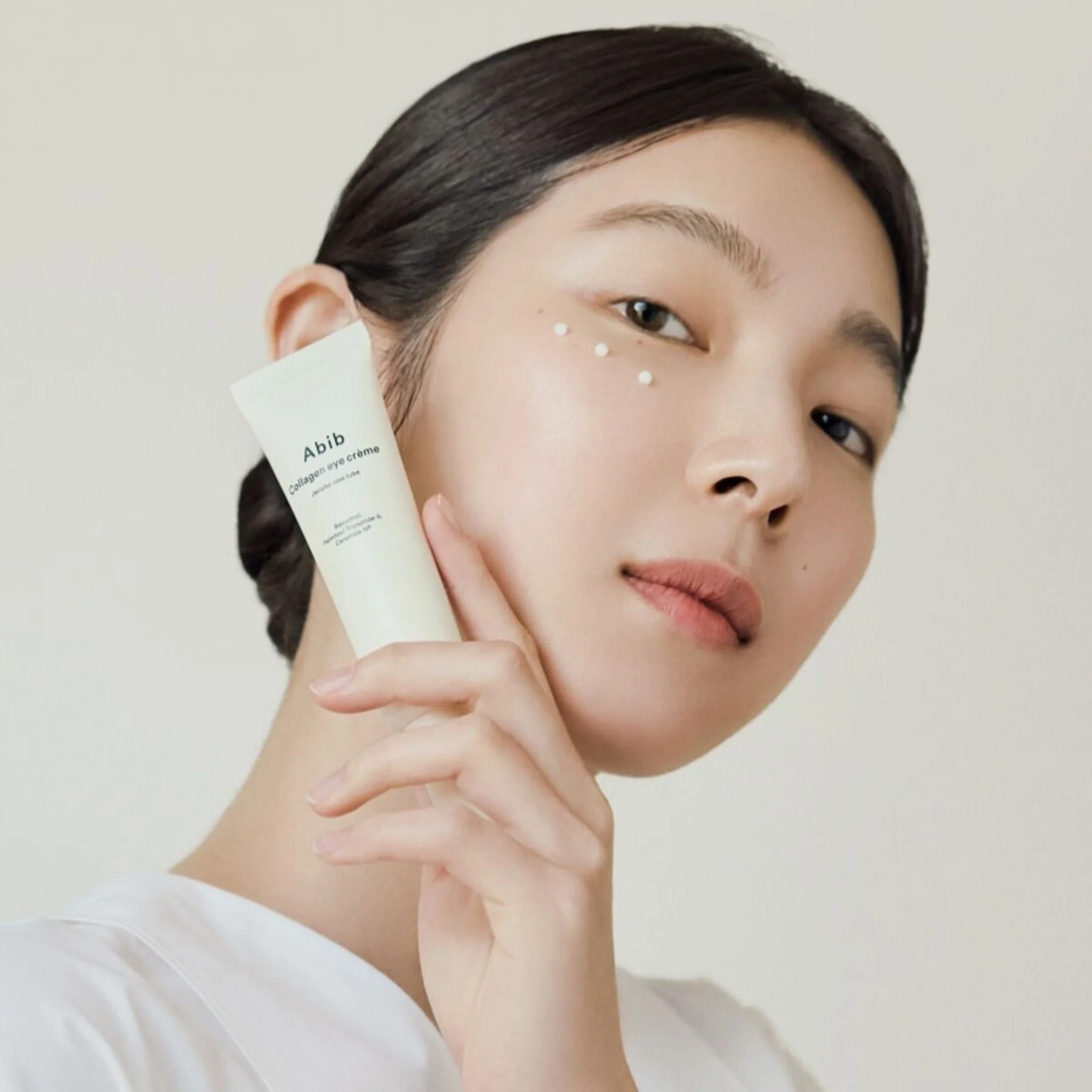 ABIB Collagen Eye Cream Jericho Rose Tube 30ml : femme applique une crème contour des yeux sur peau claire, fond clair.