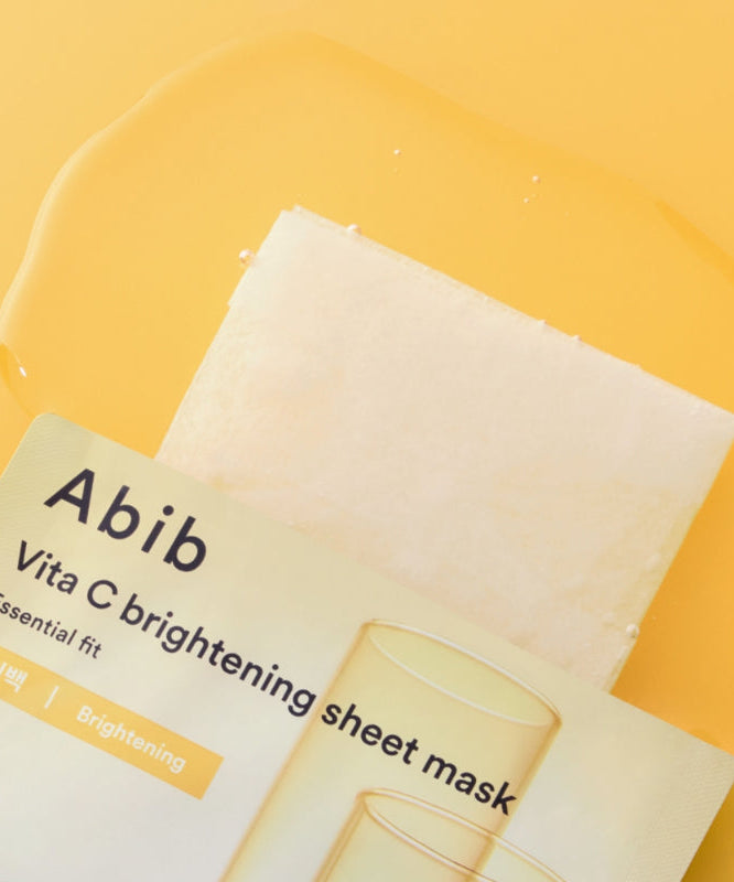 ABIB Essential Fit Vita C Brightening Sheet Mask d’Abib, masque en tissu sur fond jaune, packaging visible, vue rapprochée.