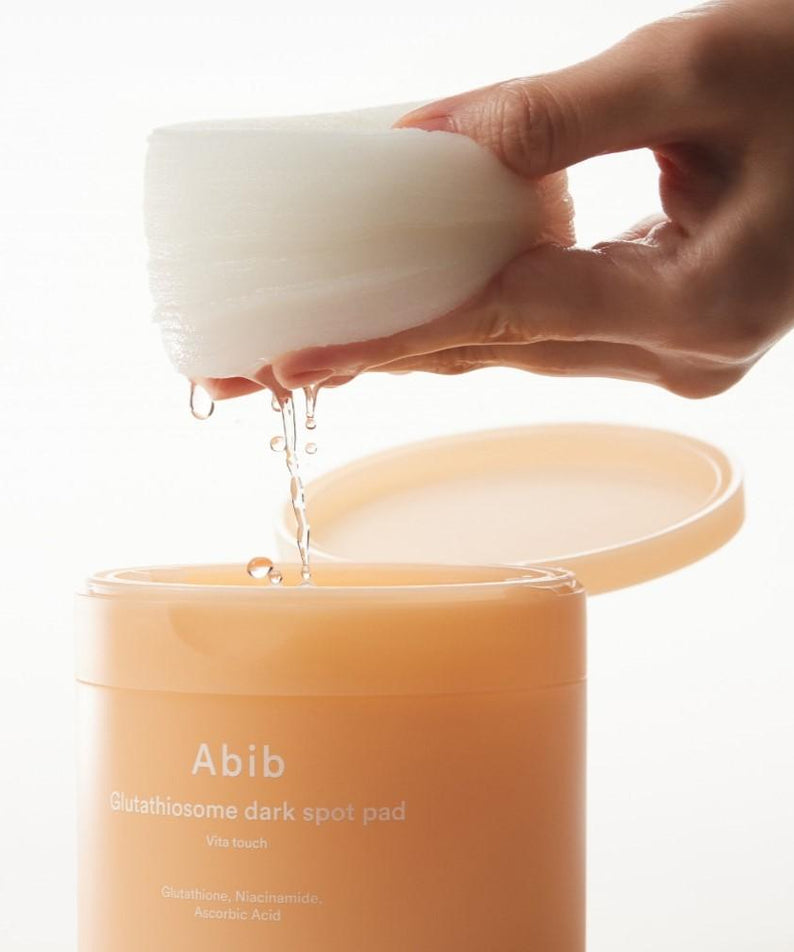 Photo en gros d’une main tenant ABIB Glutathiosome Dark Spot Pad Vita Touch 60 EA, marque Abib, face crème sur fond clair