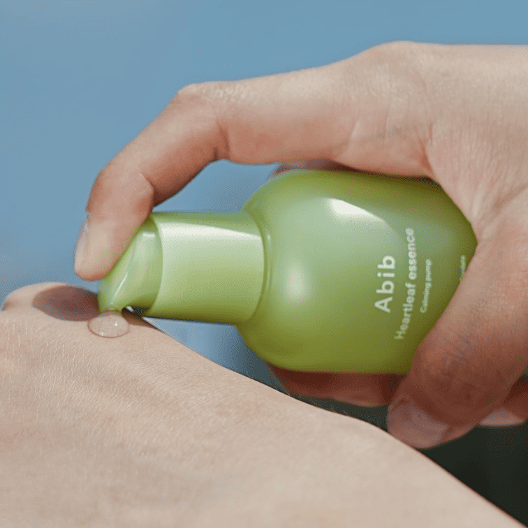Main tenant ABIB  Heartleaf Essence Calming Pump 50ml, flacon vert sur peau, ambiance apaisante, soin visage ABIB
