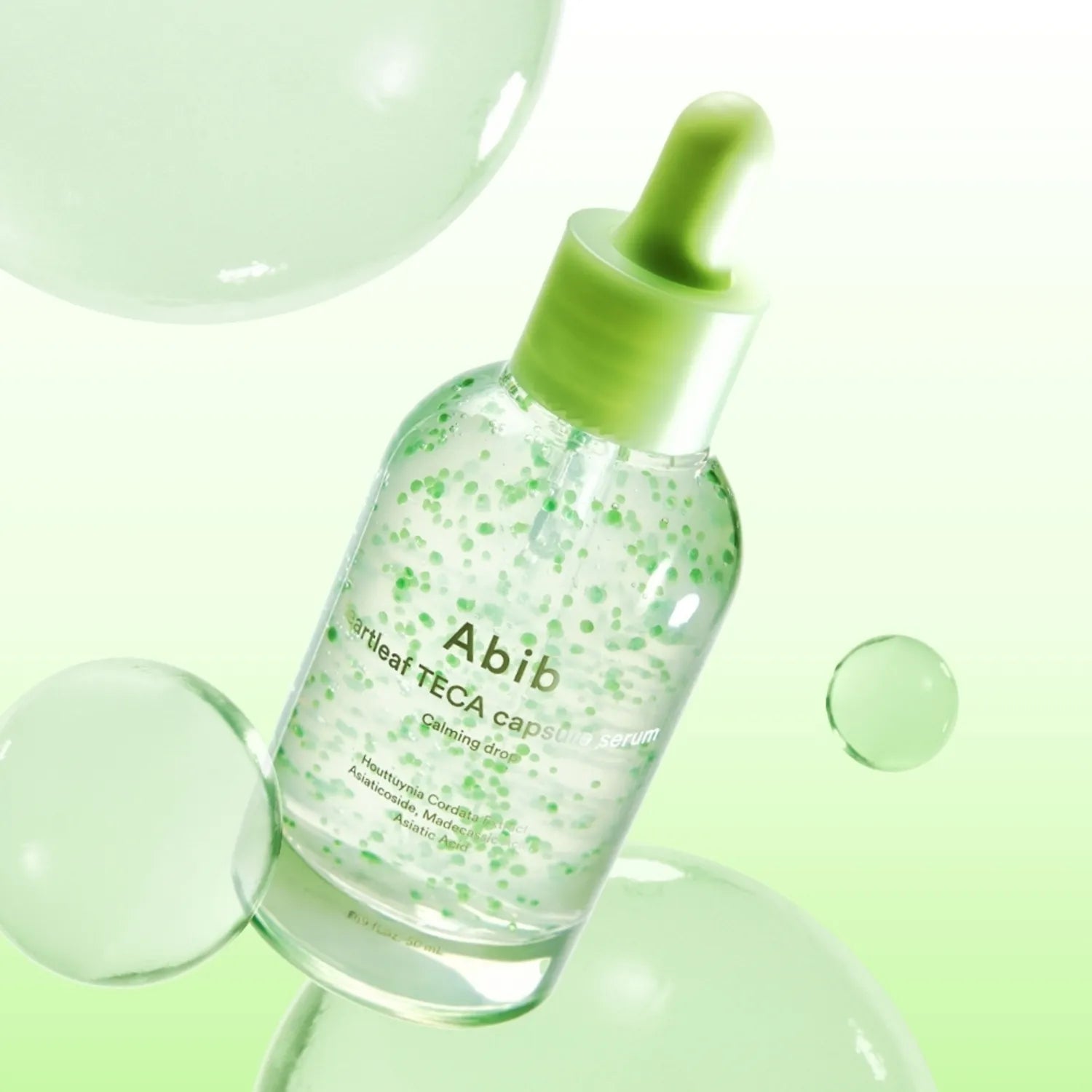 Décris l'image en français : ABIB Heartleaf TECA Capsule Serum Calming Drop 50ml sur fond vert avec gouttes et flacon.