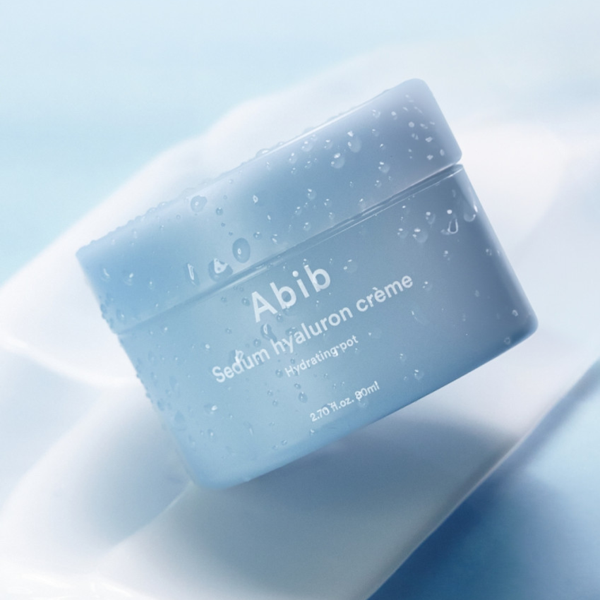 Décris l'image en français : ABIB Sedum Hyaluron Creme Hyadrating Pot 80ml, pot bleu sur fond clair avec gouttelettes.