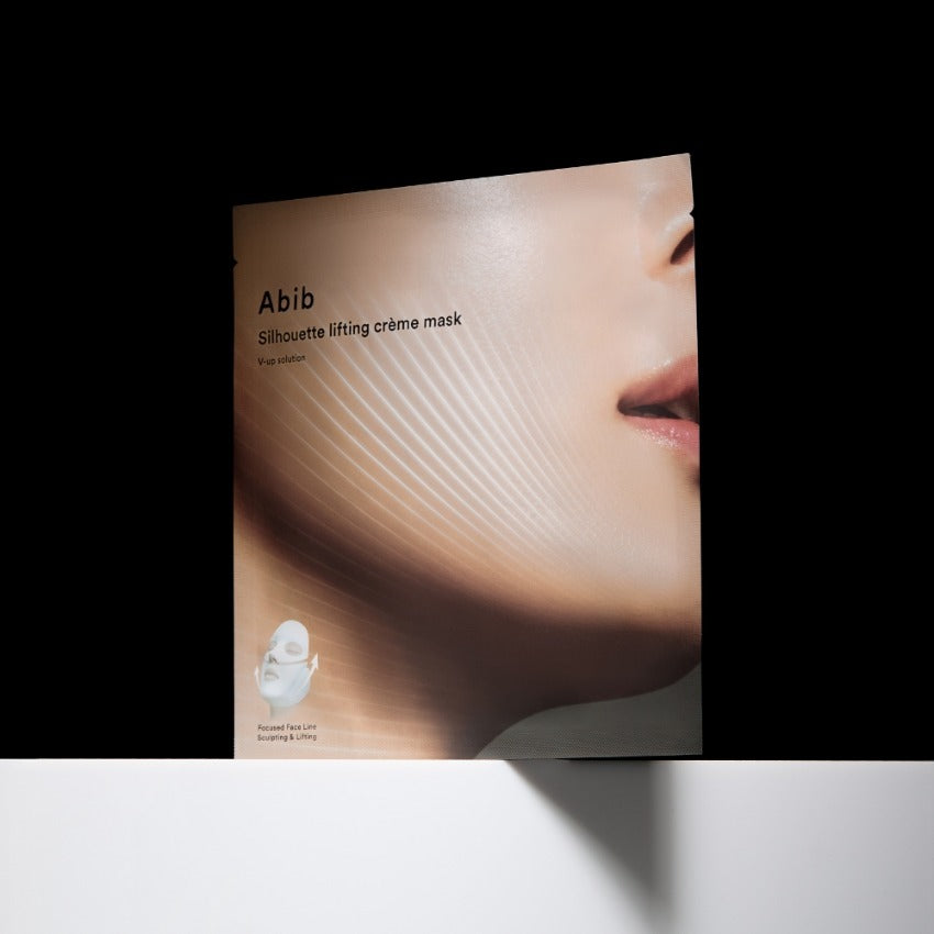 ABIB  Silhouette Lifting Cream Mask V-Up Solution, masque liftant Abib sur visage, packaging sur fond noir, lumière douce.