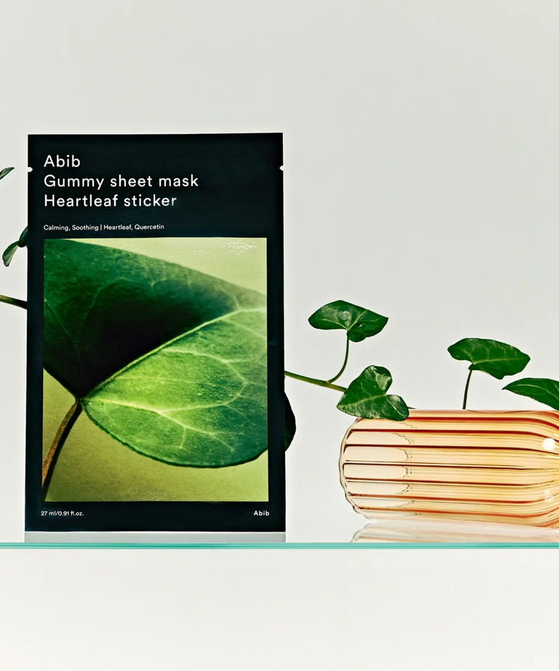 ABIB Gummy Sheet Mask Heartleaf Sticker 10 sheets sur une étagère en verre avec des feuilles vertes décoratives à côté.