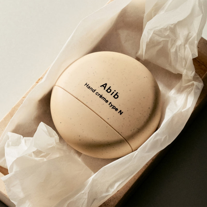 ABIB  Hand Cream Type N 50ml, crème pour les mains en photo sur fond beige avec emballage en papier froissé.