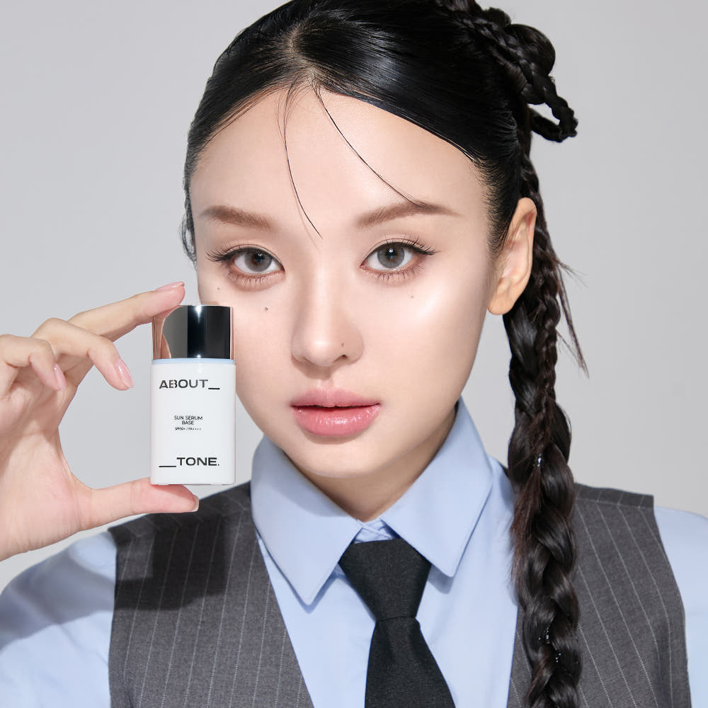 ABOUT TONE Sun Serum Base 30ml (SPF50+, PA++++), femme en tenue pro tenant le flacon, contexte beauté cosmétique