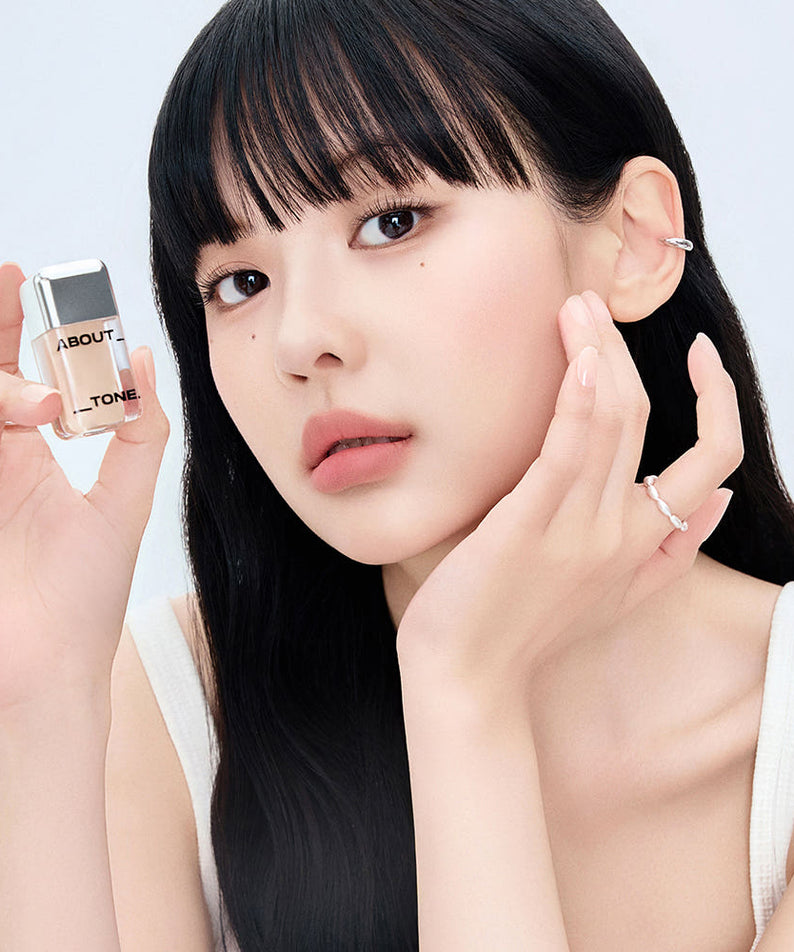 Femme tenant ABOUT TONE Skin Layer Cover Fit Concealer 5.6g, maquillage impeccablement appliqué. Concealer de haute qualité pour peau parfaite.