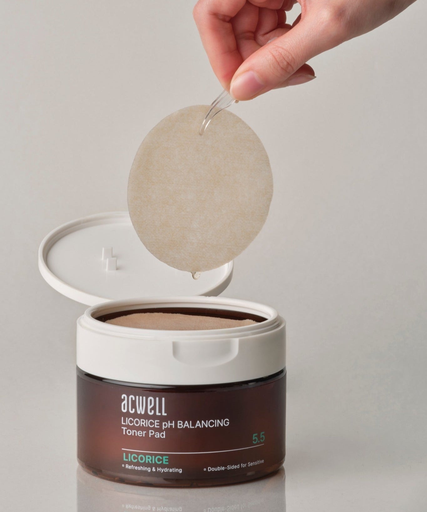 ACWELL Licorice pH Balancing Toner Pad 70P, un pot ouvert avec une main tenant un tampon, soin du visage pour équilibrer le pH.