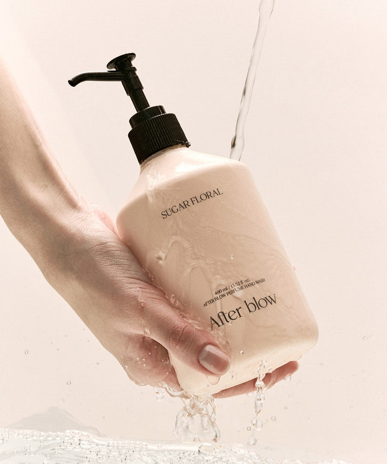Flacon de AFTER BLOW Perfume Hand Wash Sugar Floral 400ml tenu à la main sous l'eau coulant, ambiance élégante et délicate.