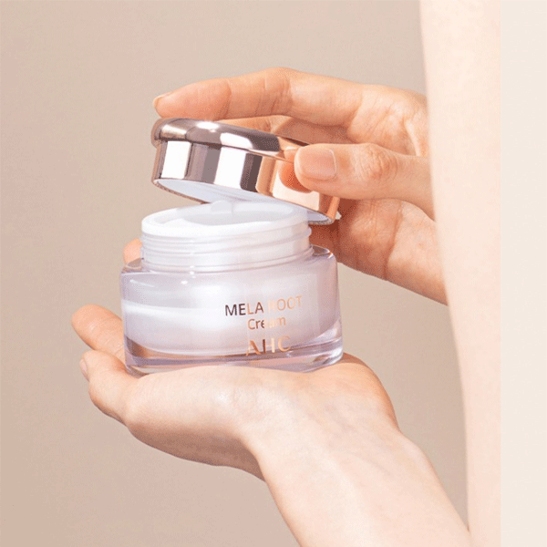 AHC H Mela Root Cream 50ml, pot crème tenu en mains, application visage, marque AHC, contexte salle de bain