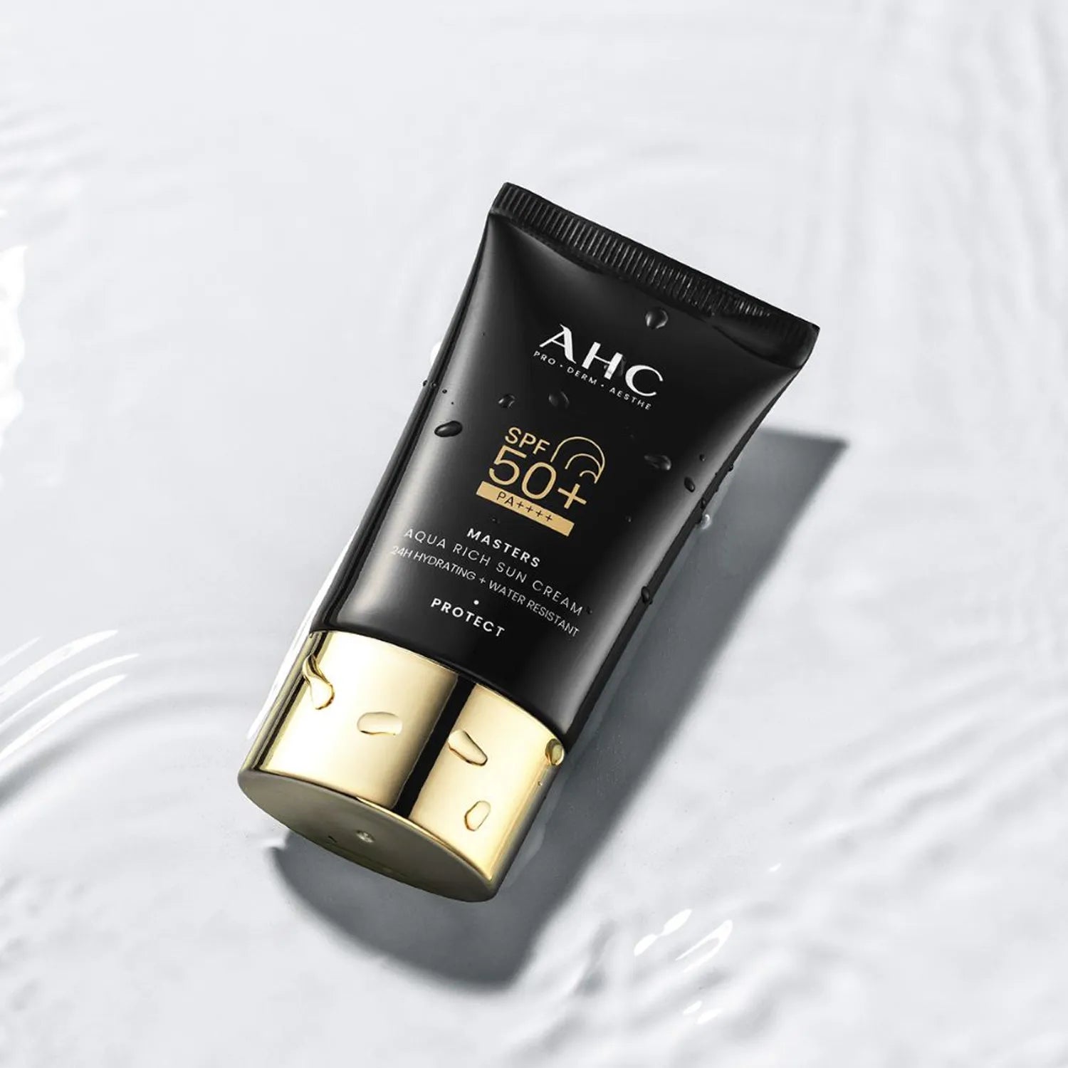 AHC Masters Aqua Rich Sunscreen 50ml de AHC, tube noir SPF 50+ sur fond clair avec gouttelettes d’eau, visuel produit.
