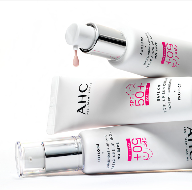 Décris l'image en français : AHC Safe On Tone-Up Sunscreen 50ml d’AHC, tubes et flacon de crème solaire à l’arrière-plan clair.