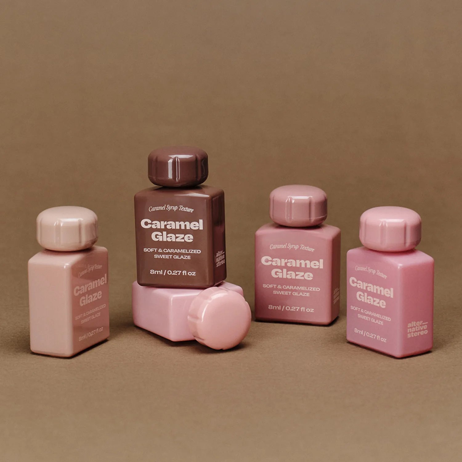 Décris l'image en français : ALTERNATIVE STEREO Lip Potion Caramel Glaze (7 colors), flacons caramel, fond beige.