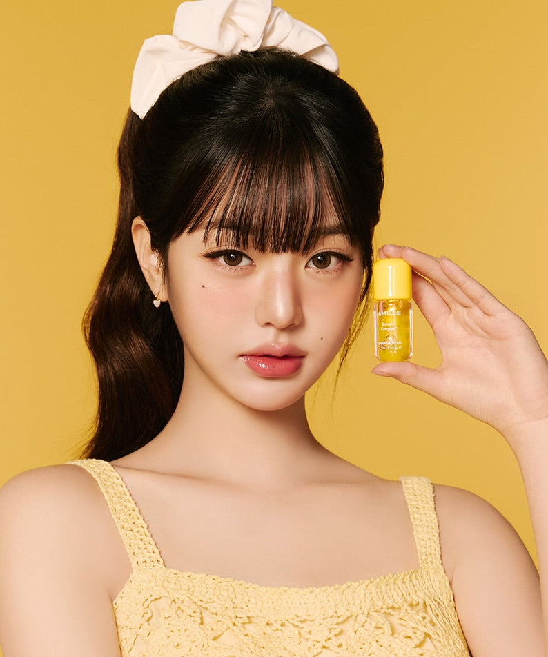 AMUSE Banana Lip Oil 4.5ml, huile pour les lèvres AMUSE, sur modèle tenant le flacon jaune sur fond jaune (studio)