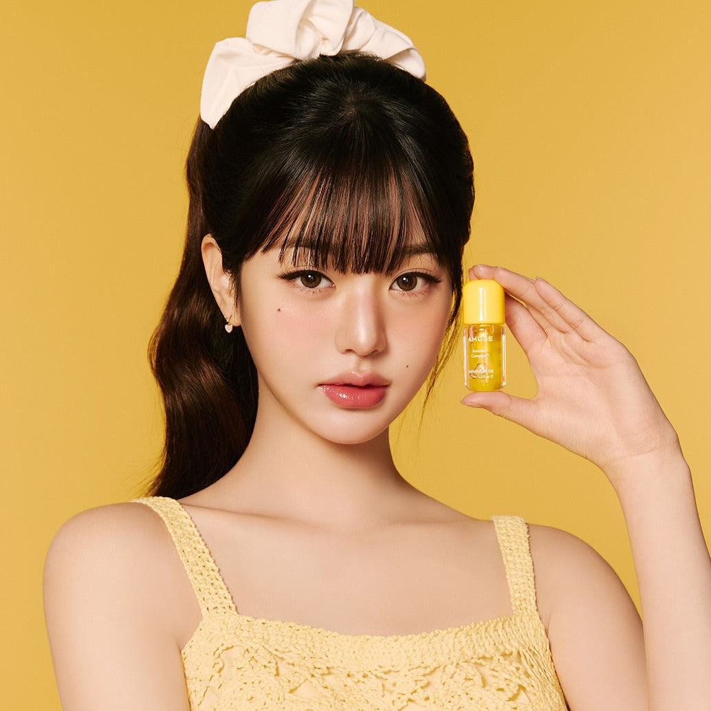 AMUSE Banana Lip Oil 4.5ml, huile pour les lèvres AMUSE, sur modèle tenant le flacon jaune sur fond jaune (studio)