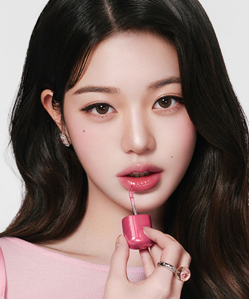 Femme appliquant AMUSE Jel Fit Gloss sur les lèvres, mettant en valeur un maquillage élégant et lumineux avec le produit AMUSE Jel Fit Gloss.