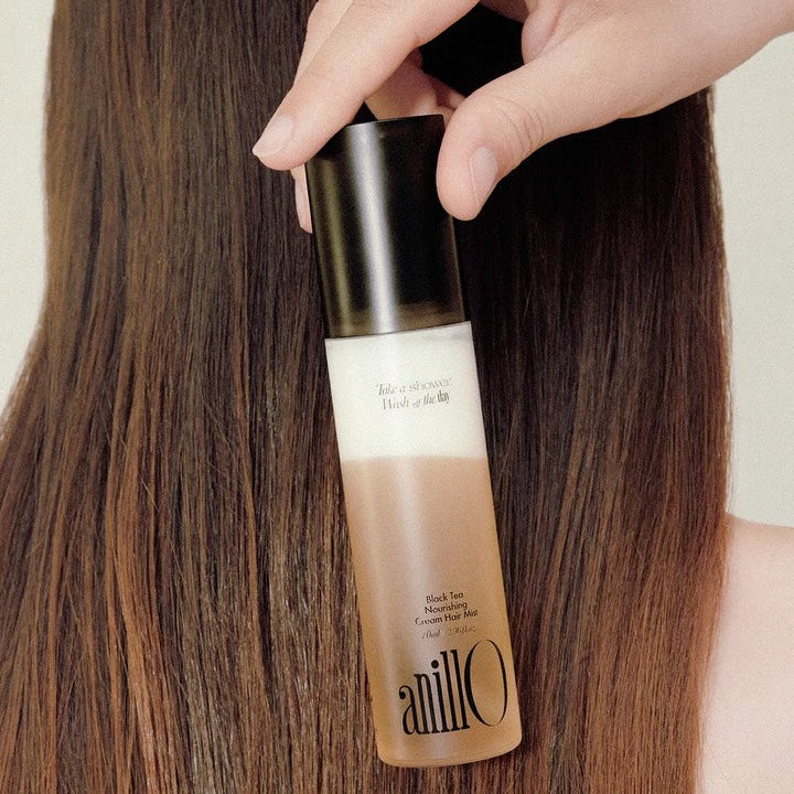 ANILLO Black Tea Nourishing Cream Hair Mist 70ml : main appliquant la brume sur cheveux bruns, flacon noir et beige