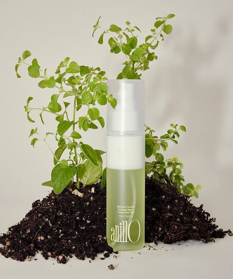 ANILLO Patchouli Garden Damage Repair Cream Hair Mist 70ml de la marque ANILLO, flacon près de plantes et terre.