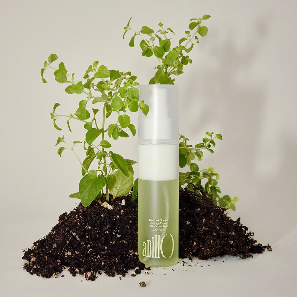 ANILLO Patchouli Garden Damage Repair Cream Hair Mist 70ml de la marque ANILLO, flacon près de plantes et terre.