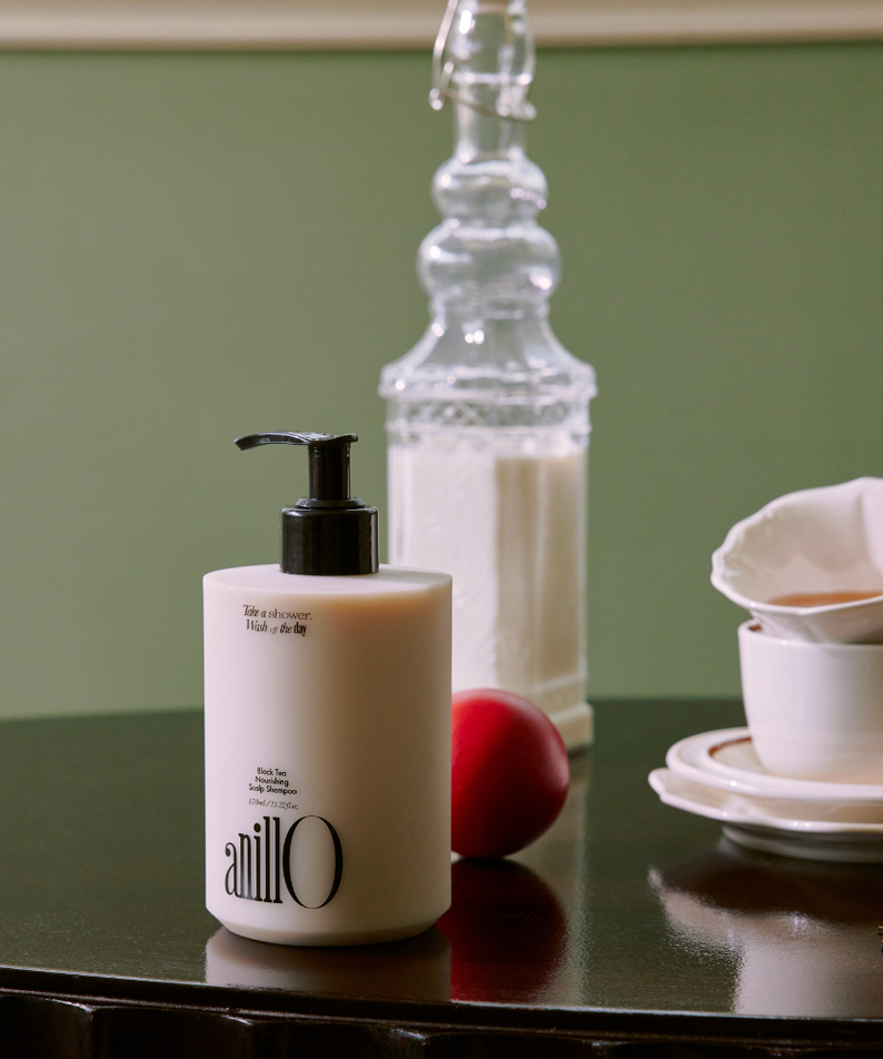 ANILLO Black Tea Nourishing Scalp Shampoo 450ml, flacon sur table verte avec éléments bain spa, contexte visuel produit
