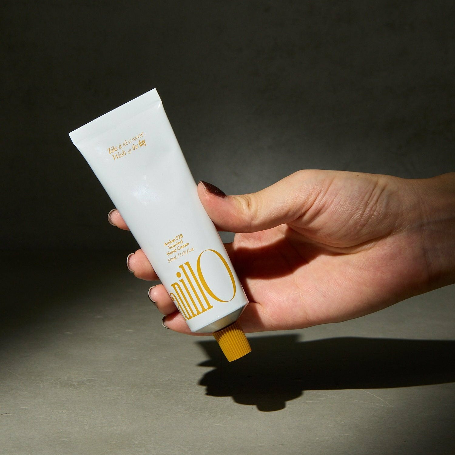 ANILLO Amber528 Scented Hand Cream 50ml en main, tube blanc et ambiance sobre sur fond gris foncé, marque ANILLO