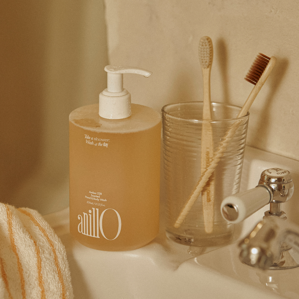 Décris l'image en français : ANILLO Amber528 Scented Hand & Body Wash 450ml, marque sur flacon, salle de bain beige.