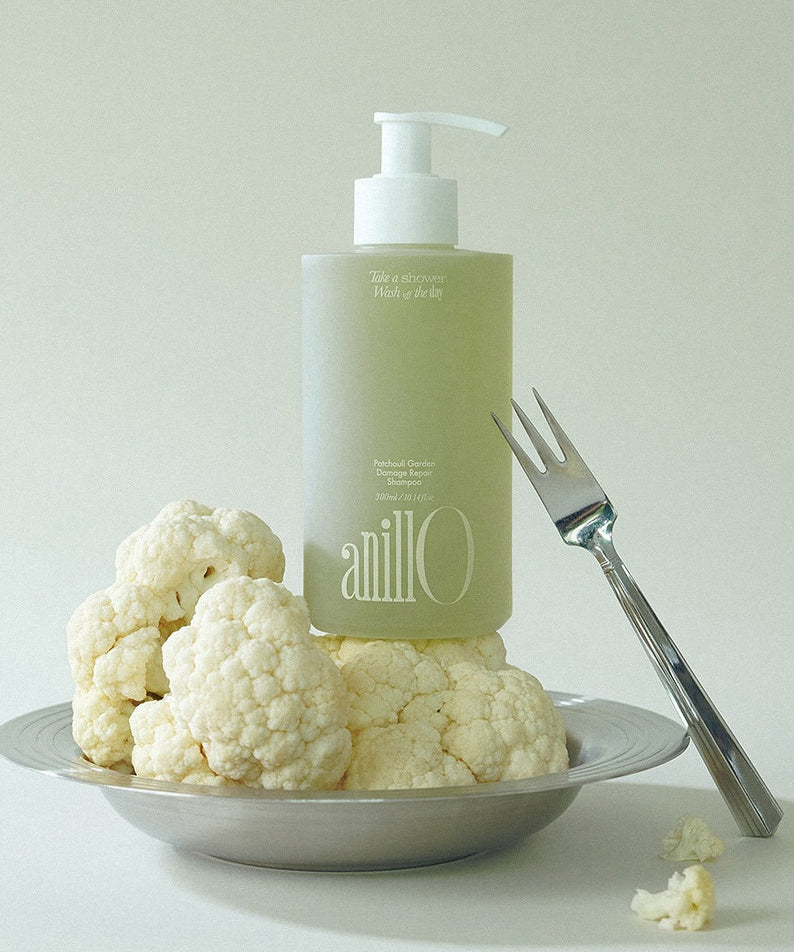 ANILLO Patchouli Garden Damage Repair Shampoo 300ml de la marque Anillo, flacon vert sur assiette blanche avec fleurs.