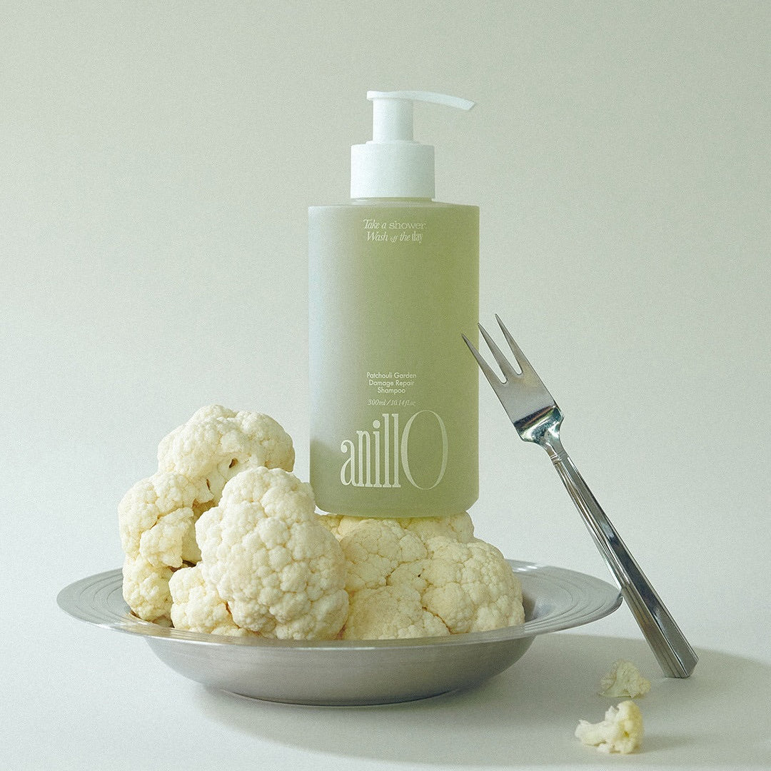 ANILLO Patchouli Garden Damage Repair Shampoo 300ml de la marque Anillo, flacon vert sur assiette blanche avec fleurs.