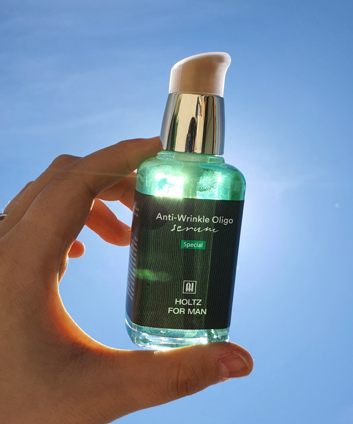 Main tenant ANNA HOLTZ For MenOligo Force Serum 60ml, flacon vert sur fond bleu, marque HOLTZ visible