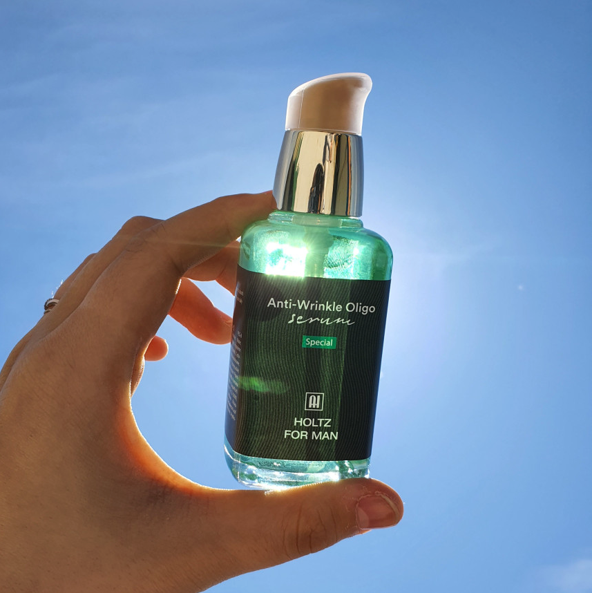 Main tenant ANNA HOLTZ For MenOligo Force Serum 60ml, flacon vert sur fond bleu, marque HOLTZ visible