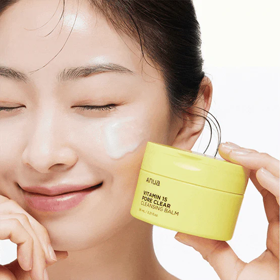 Décris l'image en français : ANUA Vitamin 15 Pore Clear Cleansing Balm 95ml, la femme applique le baume sur le visage, pot jaune.