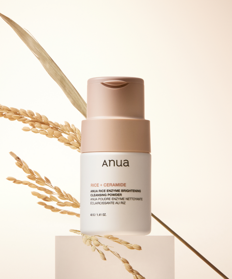 ANUA Rice + Ceramide Brightening Cleansing Powder 40g, marque ANUA, flacon crème sur podium avec grains de riz en arrière-plan.