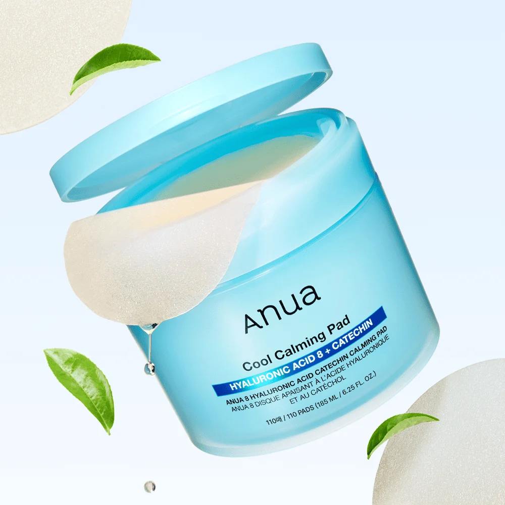 Décris l'image en français : ANUA 8 Hyaluronic Acid Catechin Calming Pads 110 Pads, marque ANUA, pot bleu, feuilles vertes.