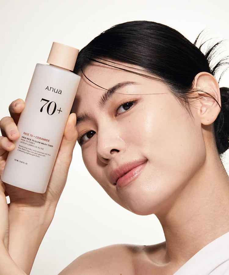 Décris l’image en français : ANUA Rice 70 + Ceramide Glow Milky Toner 250ml d’ANUA, sur une femme au visage, fond clair.