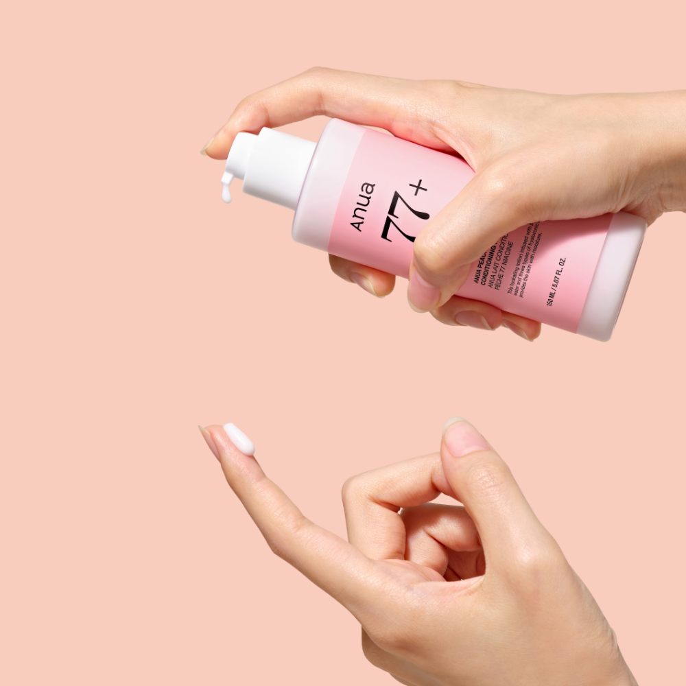 Décris l'image en français : ANUA Peach 77 + Niacin Conditioning Milk 150ml de la marque ANUA, mains appliquant sur peau.