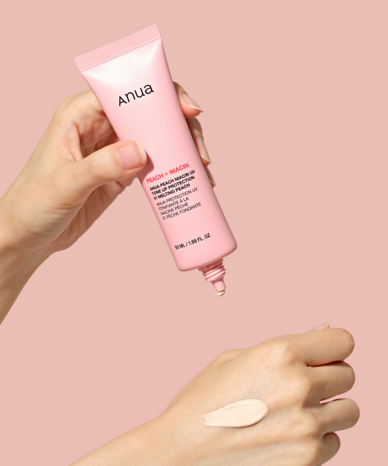 ANUA Peach + Niacin UV Tone Up Protection 50ml, marque Anua, tube crème et main avec texture, fond rose, contexte maquillage.