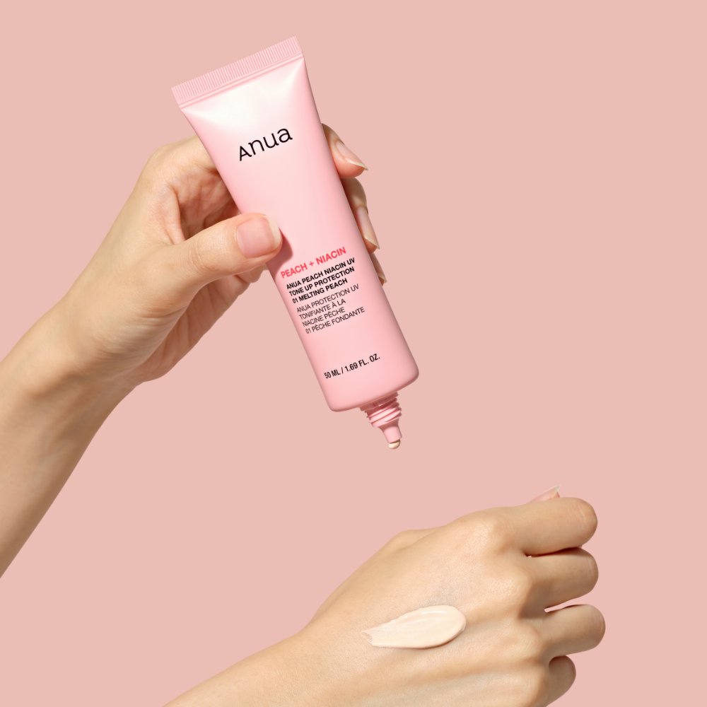 ANUA Peach + Niacin UV Tone Up Protection 50ml, marque Anua, tube crème et main avec texture, fond rose, contexte maquillage.