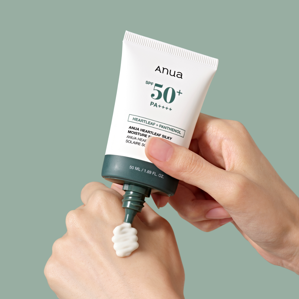 Main tenant ANUA Heartleaf Silky Moisture Sun Cream 50ml, tube crème solaire Anua, arrière-plan vert uni.
