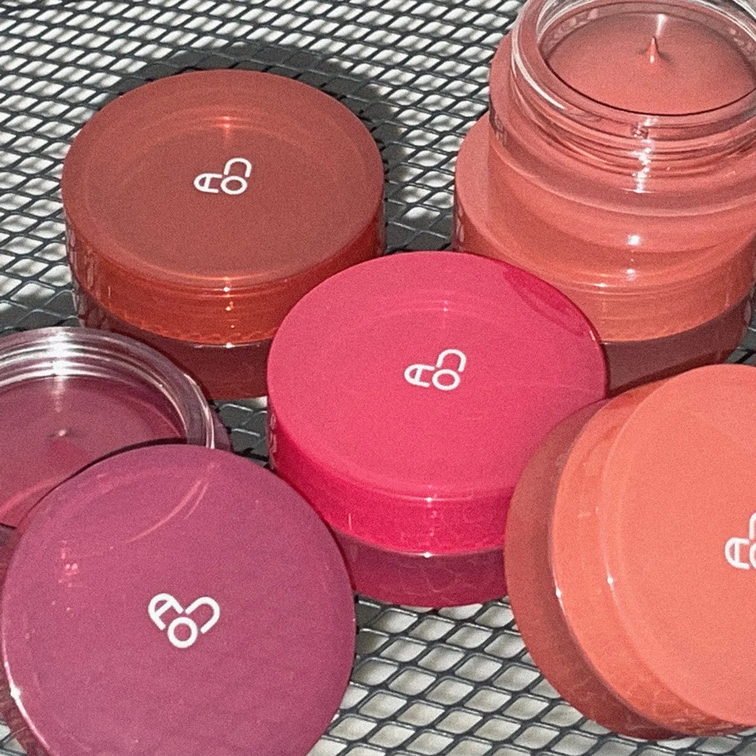 AOU Floofy Matte Balm de la marque AOU, baumes mats colorés en pots sur filet métallique, ambiance maquillage