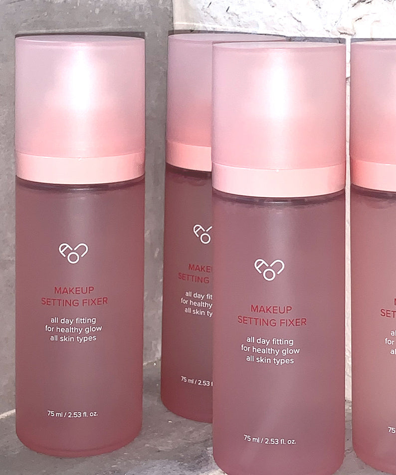 AOU - Makeup Setting Fixer 75ml, AOU Cosmetics, spray fixateur maquillage rose, pack sur fond béton gris, flacons alignés.
