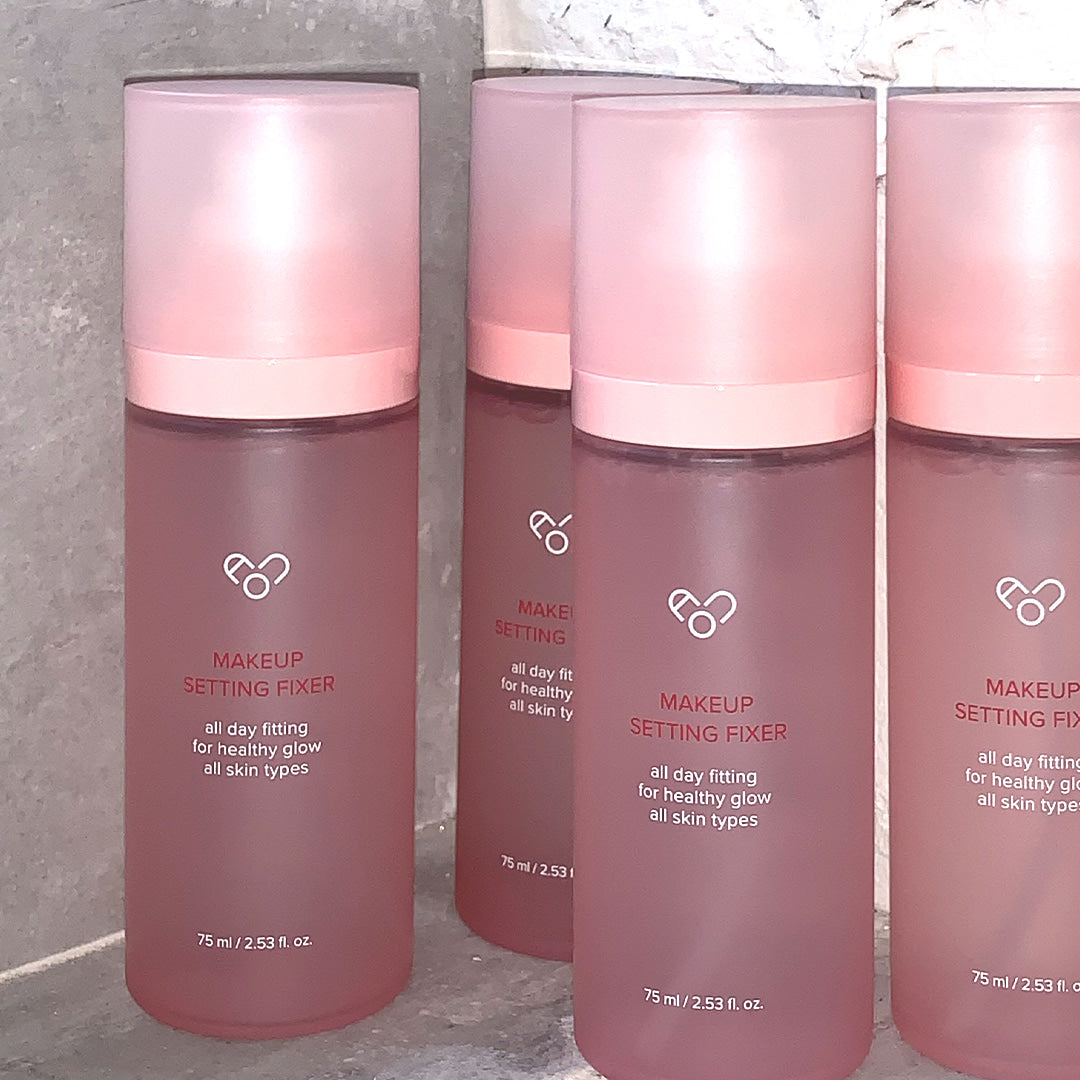 AOU - Makeup Setting Fixer 75ml, AOU Cosmetics, spray fixateur maquillage rose, pack sur fond béton gris, flacons alignés.