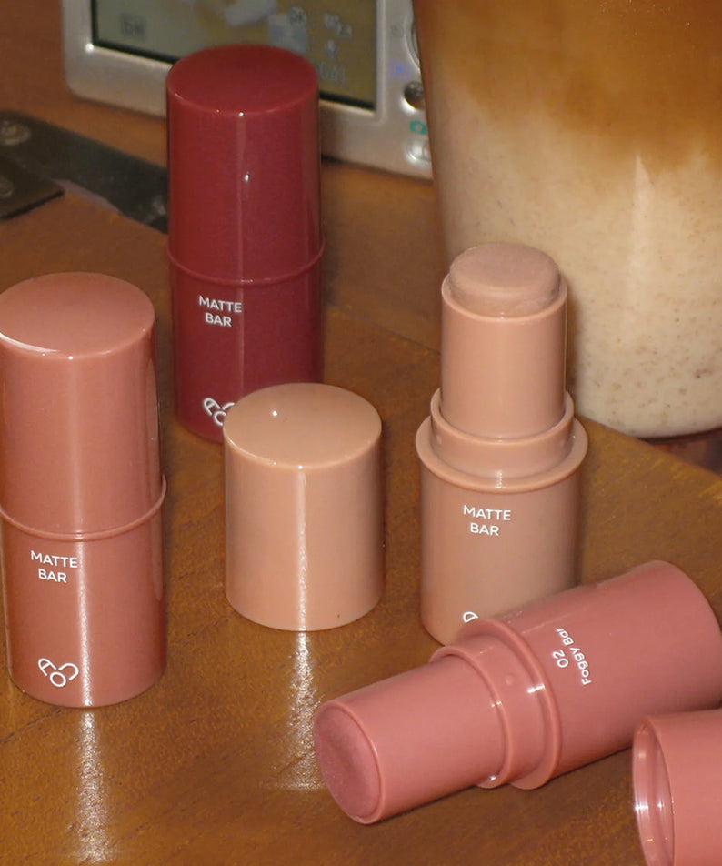 AOU Matte Bar de la marque AOU, sticks maquillage mats sur comptoir beige, ambiance salle de bain.