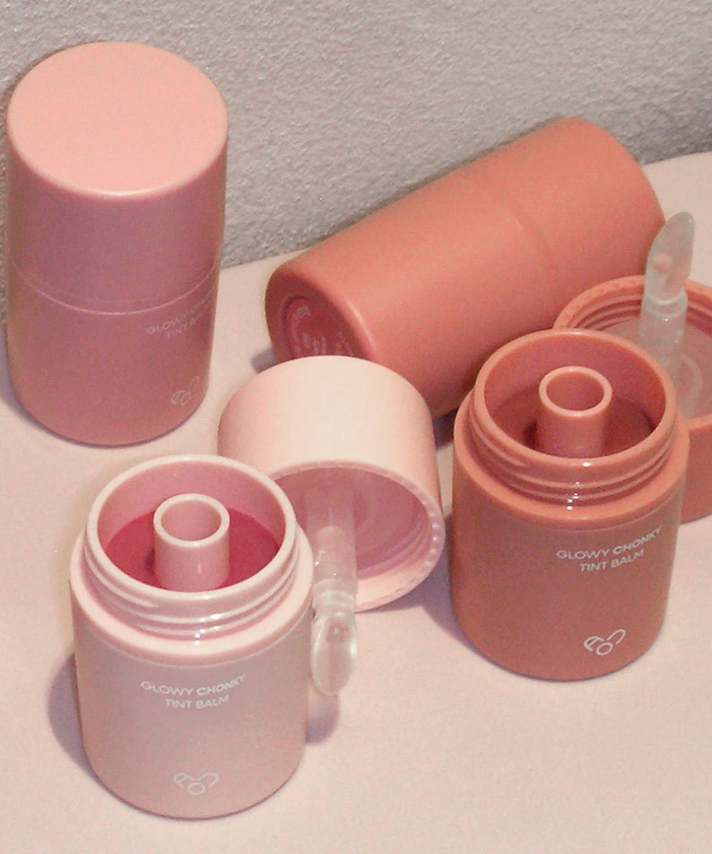 Décris l'image en français : AOU Glowy Chonky Tint Balm, baume teinté glowy de la marque AOU, pots roses sur fond clair
