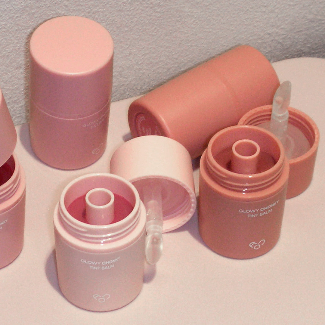 Décris l'image en français : AOU Glowy Chonky Tint Balm, baume teinté glowy de la marque AOU, pots roses sur fond clair