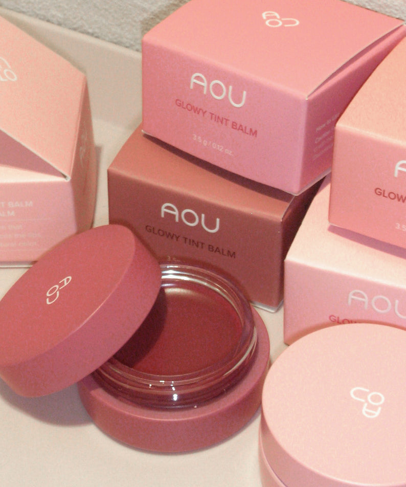 AOU Glowy Tint Balm, coffrets roses et baume luisant dans un contexte de comptoir maquillage, marque AOU
