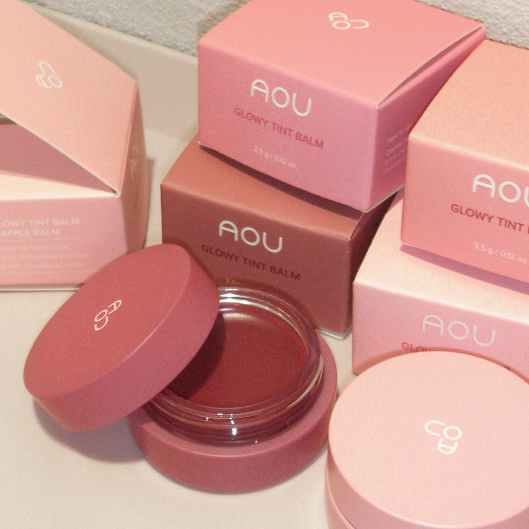 AOU Glowy Tint Balm, coffrets roses et baume luisant dans un contexte de comptoir maquillage, marque AOU