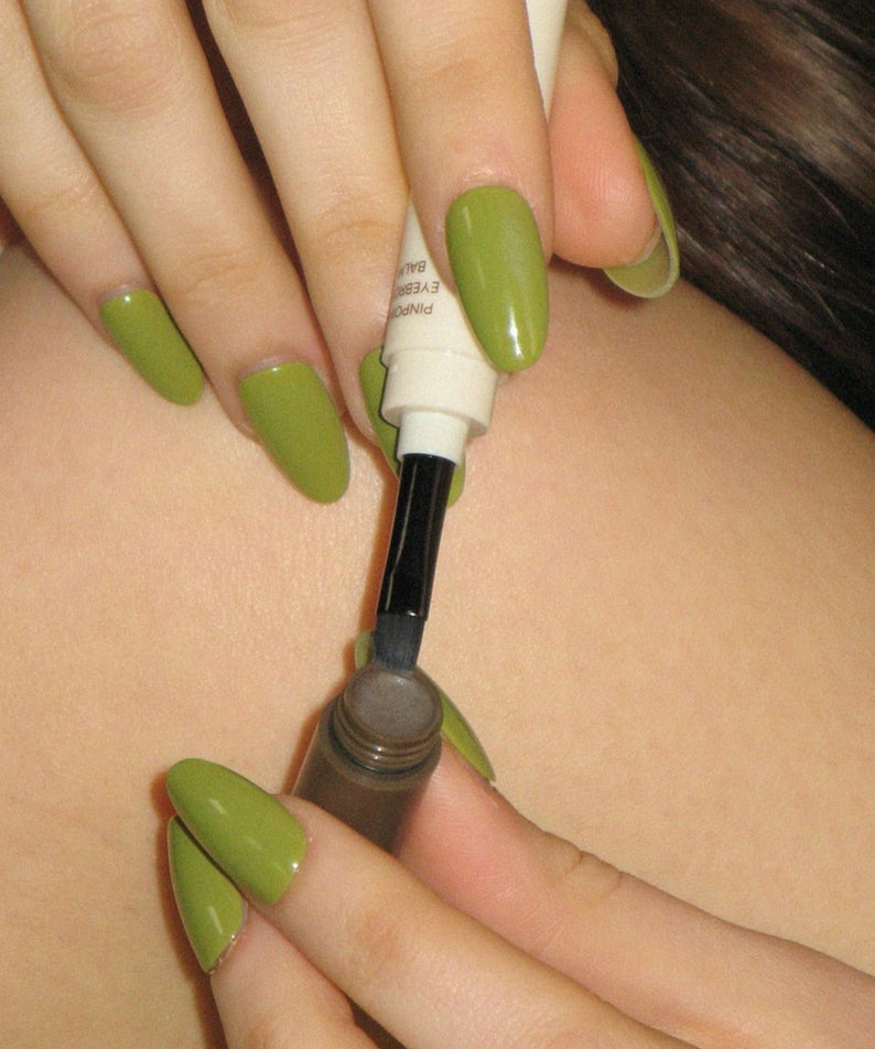 Application du AOU Pinpoint Eyebrow Balm avec un pinceau, mettant en valeur des sourcils définis et élégants.