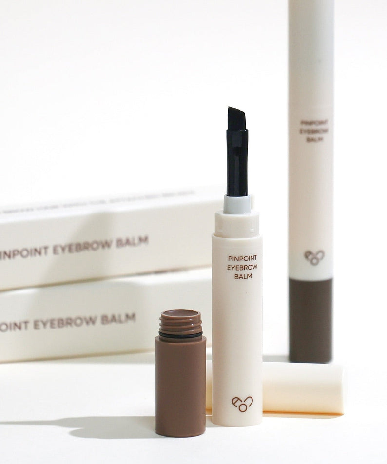 AOU Pinpoint Eyebrow Balm en présentation élégante avec son applicateur unique et ses boîtes en arrière-plan.