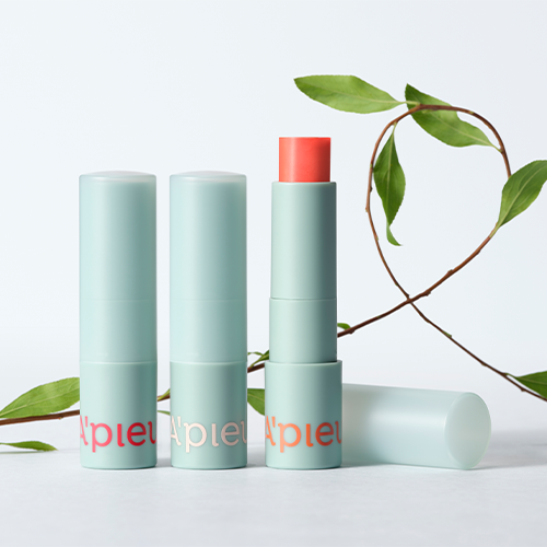 A'PIEU Juicy Pang Care Lip Balm de la marque A'PIEU, packaging vert menthe, feuillage sur fond clair, photo produit en studio.